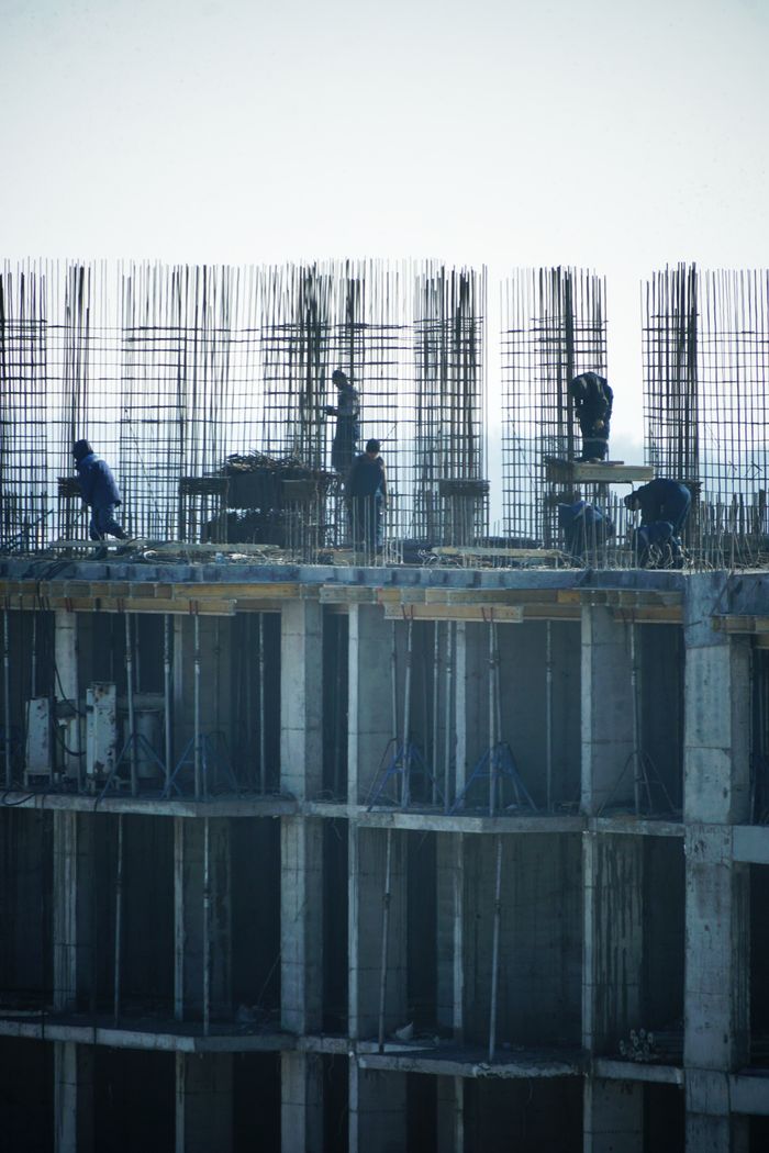 Construction workers at a high-rise building site with visible steel reinforcements.
