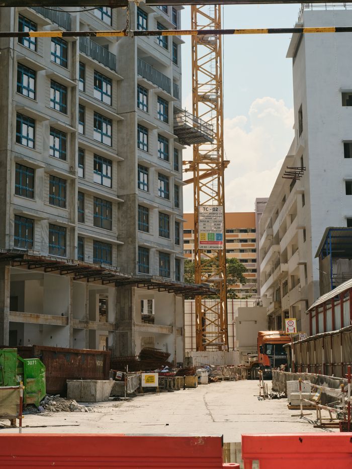 A bustling urban construction site with a tower crane and surrounding buildings under a clear sky.