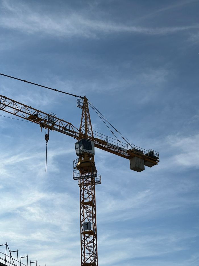 our-story Tall tower crane at a construction site with a clear blue sky background, showcasing construction industry machinery.