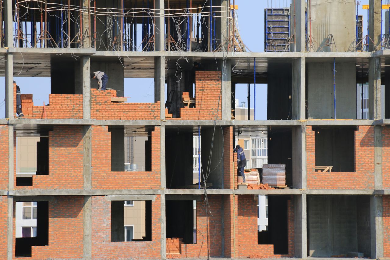 about-us Workers engaged in bricklaying on a multi-story building under construction in an urban area.