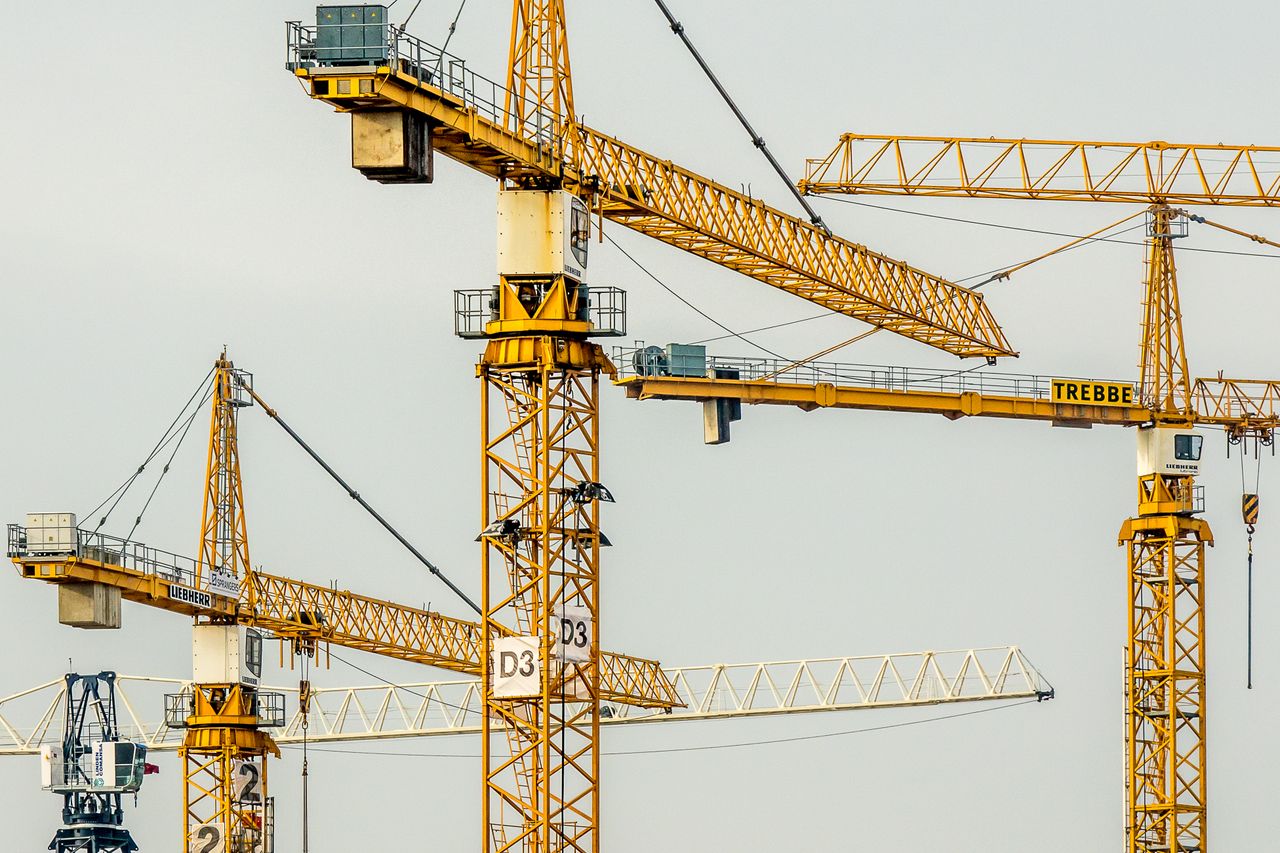 heros-img Cluster of yellow tower cranes at a construction site with a gloomy sky background.
